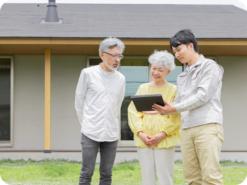 家の庭で作業着を着た従業員がタブレットの画面を指差しながら老夫婦に説明している様子