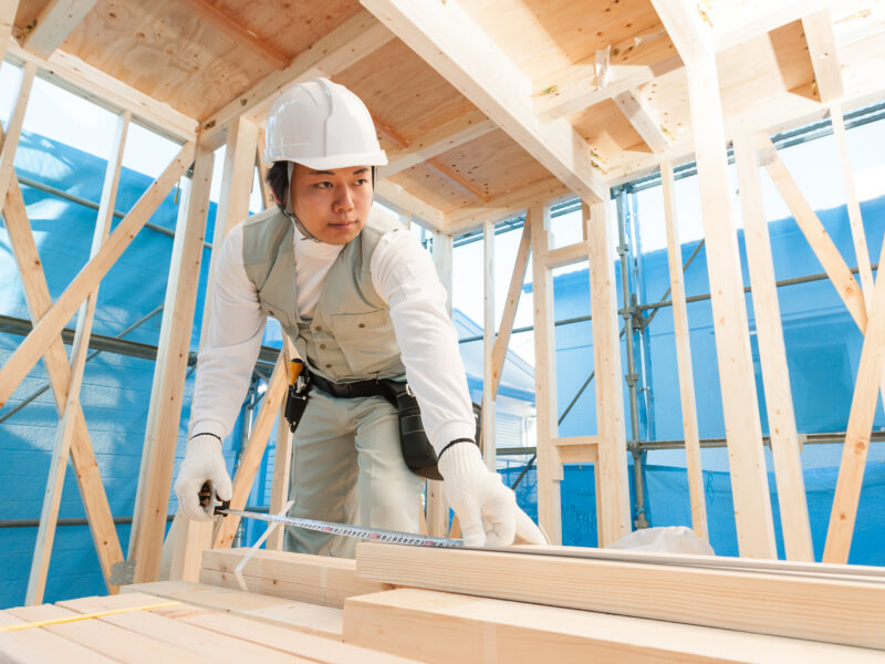大工が家の建設現場で木材の長さを測定している様子