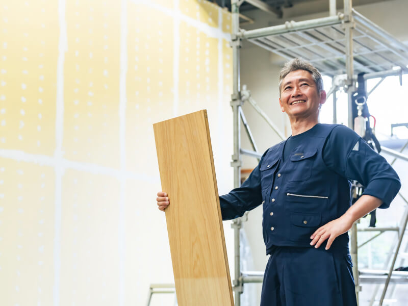 大工が建設現場で木材を右手に持ち斜め上を見ている様子