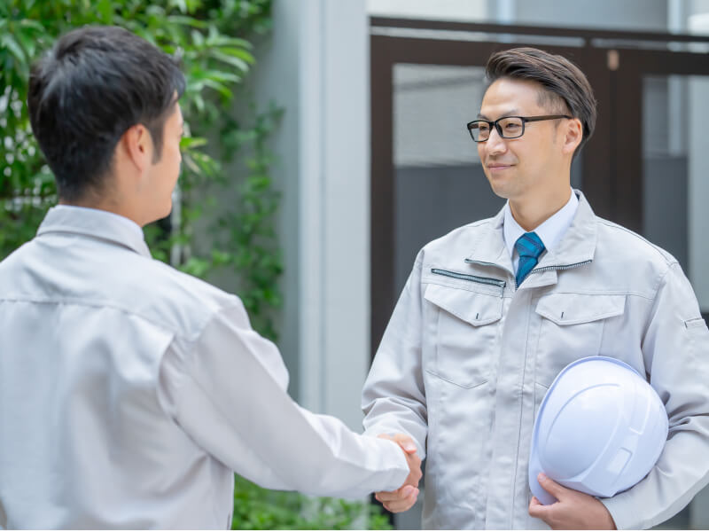 作業着を着た従業員二人が握手をしている様子