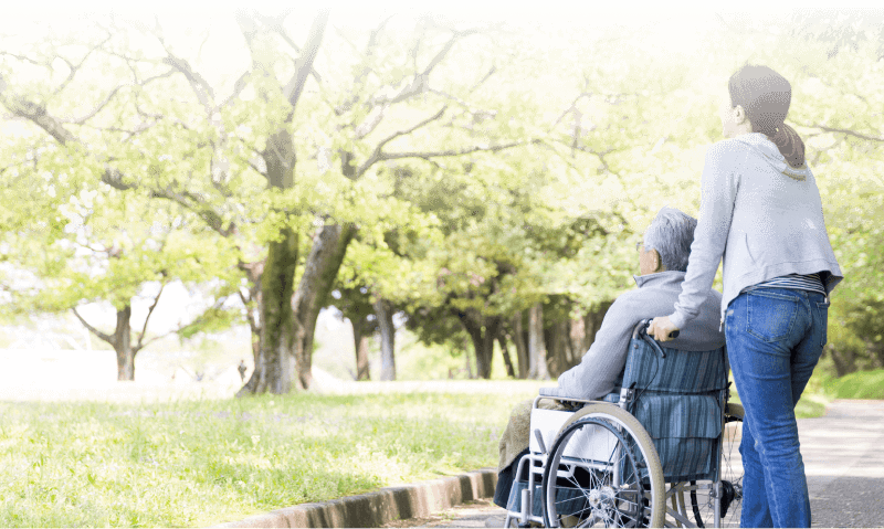 緑豊かな外に出ている車椅子の老人と介護者